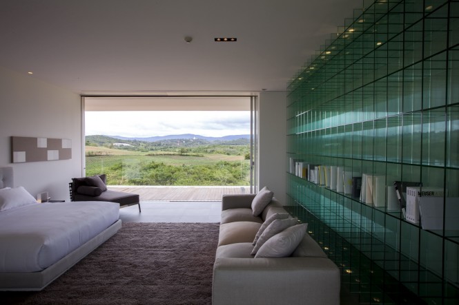 The modern bedroom offers an unusual solution for bookshelves in the form of an entire wall of sectioned glass, which also compliments the glass of the exterior walls.