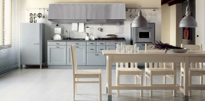 A retro kitchen is subdued in matte grey paint that resembles primer yet looks quite at home accented by the cream walls and natural finished furniture.