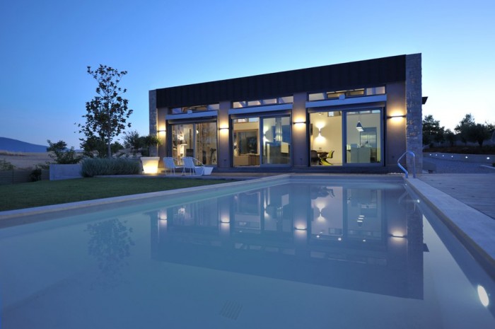 A luxuriously large swimming pool expands from just outside the home outwards.