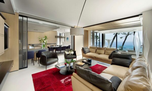 The living space is furnished with comfortable upholstered contemporary furnishings and pops of red accents.