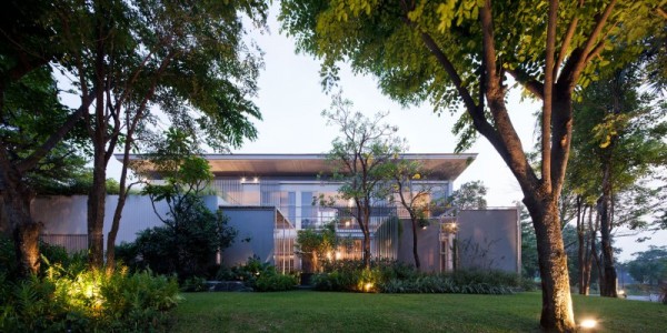 The modern house's exterior shows a boundless lawn filled with trees and greenery but no fences or walls.