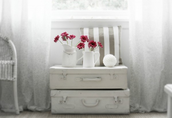 suitcase stack beneath window with crimson florals in jugs