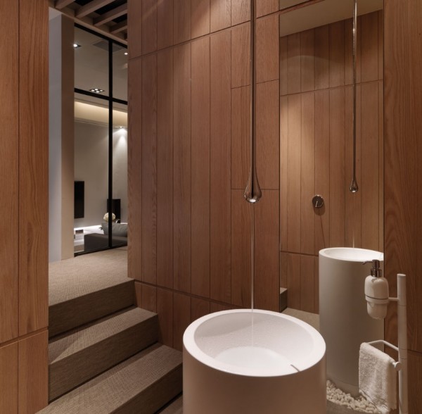 The sunken bathroom boasts rich organic walls and round shaped basin with single bulb fixture above.