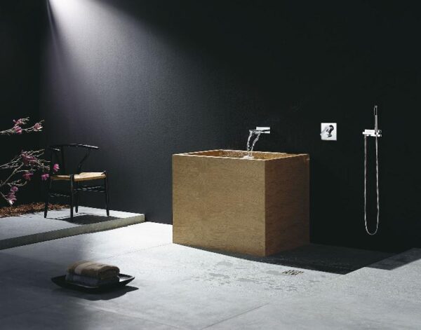 A minimalist bathroom features a single lavatory sink made of natural wood and undefined shower area highlighted dramatically by natural light streaming from above.