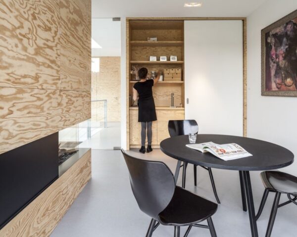 Sliding doors hide a small kitchenette with sink and pantry. A black dining table and chairs contrast nicely with the raw wood of the fireplace surround.