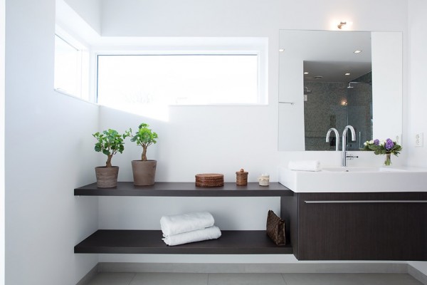 The built-ins in this modern bathroom are as aesthetically pleasing as they are functional. The dark wood of the vanity and shelves contrast nicely with the pristine white walls and floors.
