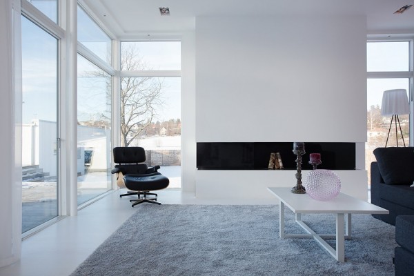 The central living room features a sleek fireplace surround with nondescript lines. An Eames Lounge Chair adds a touch of mid-century modern aesthetic.