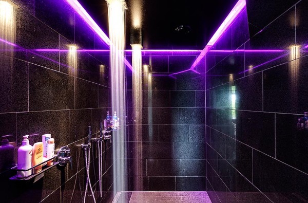 A large shower surrounded in granite tile is alight in purple florescent lights for a otherwordly feel.