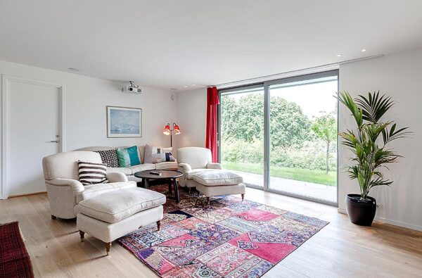 A media room is decorated in an English style with comfy armchairs and ottomans in white and beautiful patchwork rug added for interest and texture.