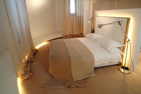 The master bedroom is filled with natural textures from woven rug to linen-look draperies and bedding. The bed's headboard is dynamically lit from behind.