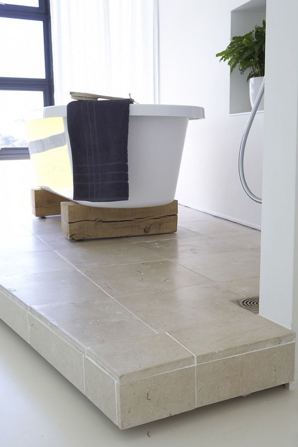 A soaking tub sits atop two aged wood blocks adding a touch of rustic charm to the bath area.