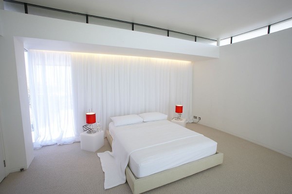 Red table lamps offer a pop of color in this all white minimalist bedroom.
