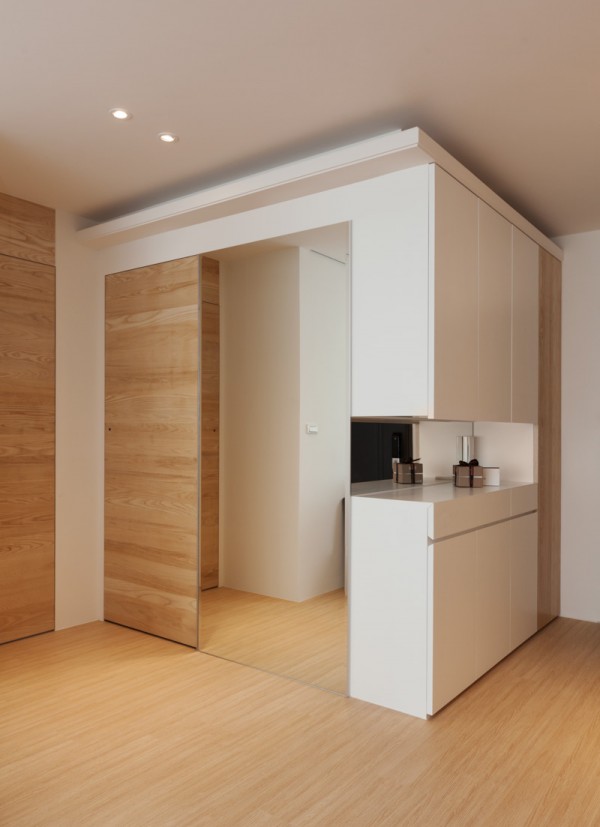 Part of this design element includes hidden storage. Cabinets and shelving are only revealed when doors that are otherwise flush with the wall are opened. This means that necessities are easily in reach, but kept out of sight unless in use. The use of pocket doors goes even further, giving the entire apartment an open and airy feeling, as if it were one big room, whenever the doors to the bedrooms are open.  Neutral tones dominate the space with complementary pops of color drawing attention in the form of teal and orange-accented chairs and a uniquely yellow oversized light fixture. These colorful elements add a bit of whimsy to an otherwise starkly calm palette and are easily switched out for a completely different look.