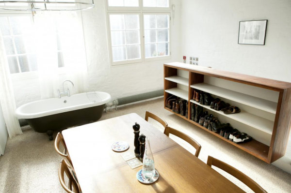 The next big space saving tactic employed in this home is a second combination space which makes up the kitchen, dining room and the bathroom. This may seem strange, but it actually works in this space. A full stand in tub was added against the wall, right next to a wall of windows and the shower curtain is also suspended from the ceiling and surrounds the entire tub for privacy. Because it is off to the side, it doesnâ€™t grab your attention immediately and it doesnâ€™t become the focal point of the room. Built in shelves make a great place for shoe storage and hidden cubbies in the wall hide the garbage can and a small refrigerator.