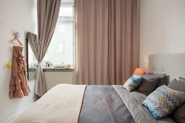 The bedroom stays true with white walls, but brings softer neutrals in with beige curtains and a charcoal duvet. The fabric headboard completes a soft and comfortable look where anyone would be happy to rest.