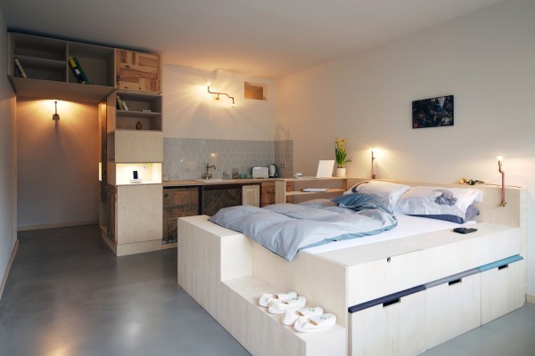 Sometimes less room means more creativity. This one room apartment makes careful use of the allotted space with a platform bedframe featuring built-in storage and an eclectically outfitted kitchenette. A mixture of reclaimed wood patterns manage to bring a whimsical interest without busying up the overall simplicity of the space.