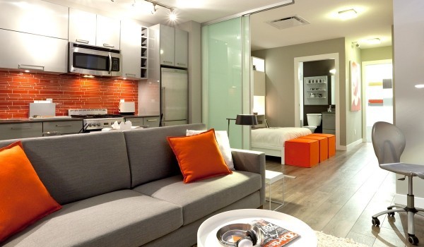 When home has an open floor plan, it is important that rooms are divided but still have a unifying design feel. Here, a bright orange backsplash is a dramatic focal point in the kitchen, while accent pillows on the couch tie everything together without being cartoonish.