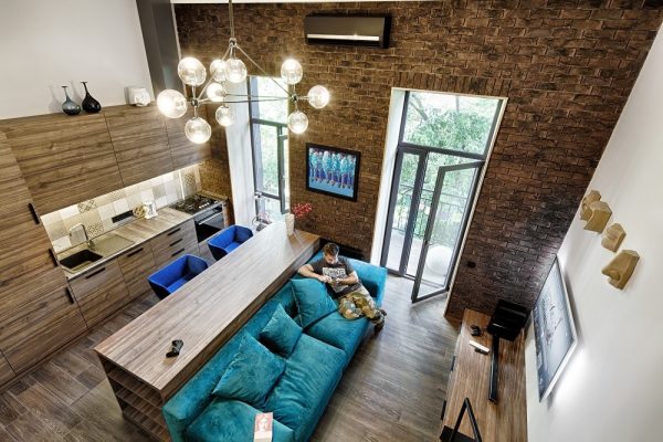 A 49-metres-squared loft in Kiev by Ivan Yunakov (https://yunakovdesign.com) also uses signature shades to create harmony in cosy spaces. High-ceilinged brick and panelled wood fixtures afford the height for long-lined doors, which are stretched horizontally by similar-shaped benches. A turquoise couch with electric blue suede single seats offer seats to look at bauble lighting, the only rounded fixture in the room.