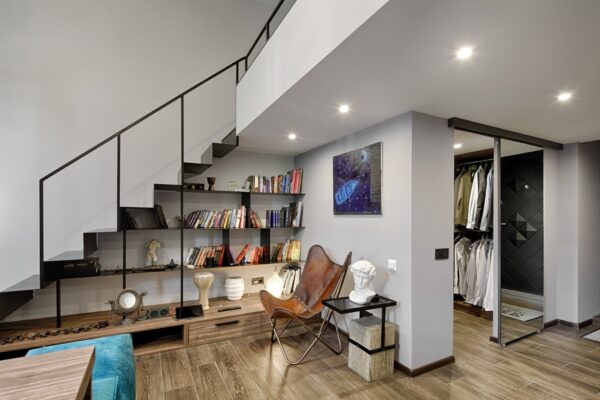 To the right, white walls offer a respite for wardrobes and bookshelves, which offer drops of colour against its simplicity. A cast iron staircase holds a frame and lets the chair, bust and painting details do the talking.