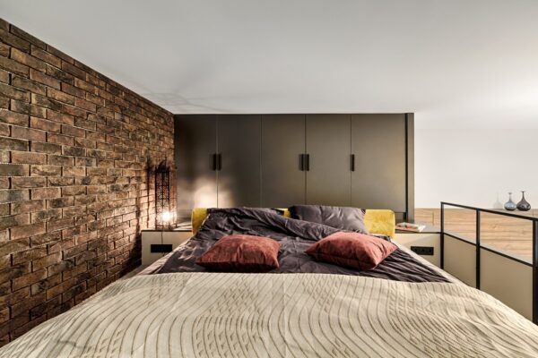 The brick façade continues into the master bedroom, where warmer tones come into play. A beige cover with terracotta and fawn cushioning is a muted place to rest one’s head, beside a mosaic light that ties in the kitchen tiling and iron staircase.