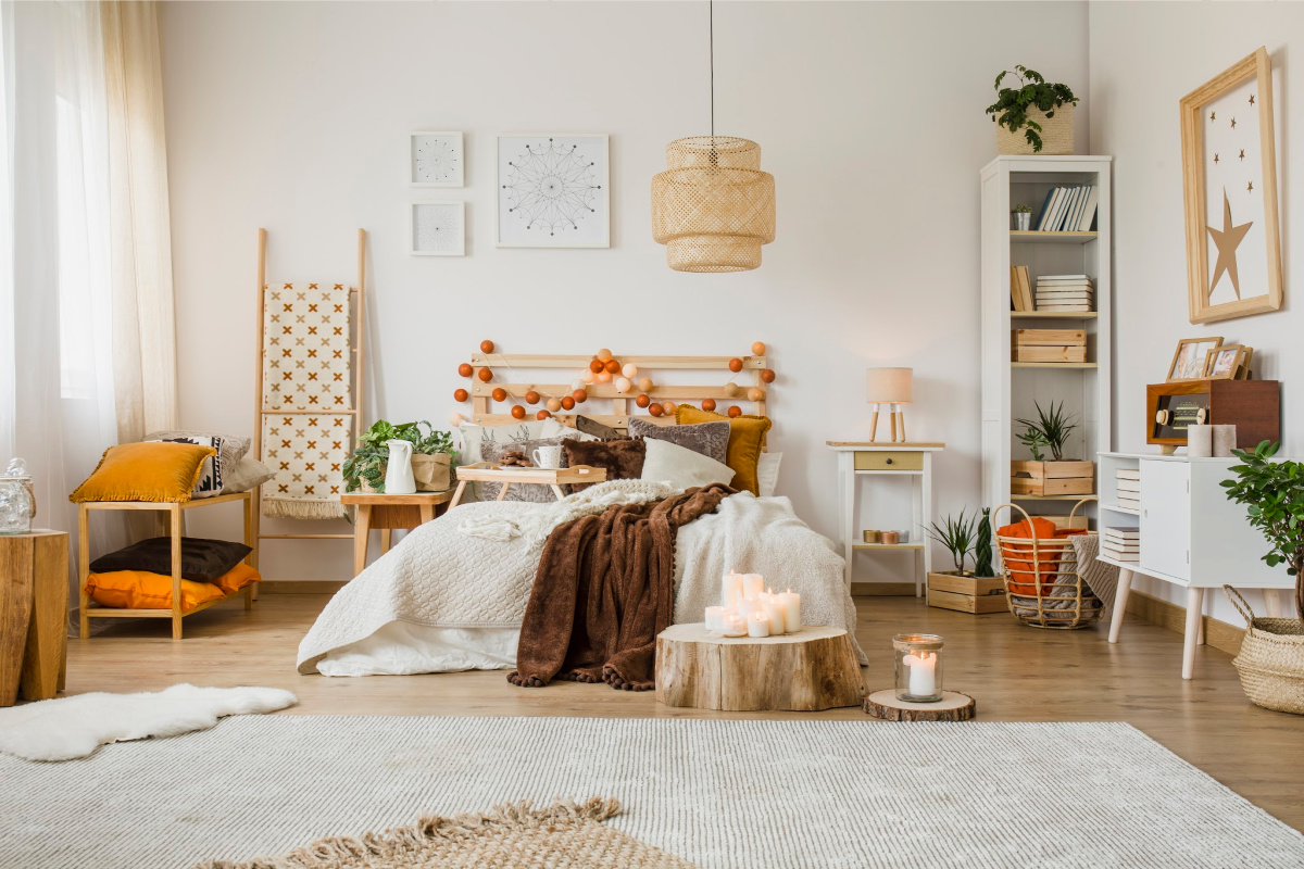 Cozy rustic bedroom with boho ethnic decor. Large windows. Double wooden bed  with many pillows and handmade textiles. Wooden furniture. Plants in the  interior. Nobody. Large windows in appartment. Stock Photo