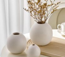 three white ceramic vases on table with dried yellow flowers